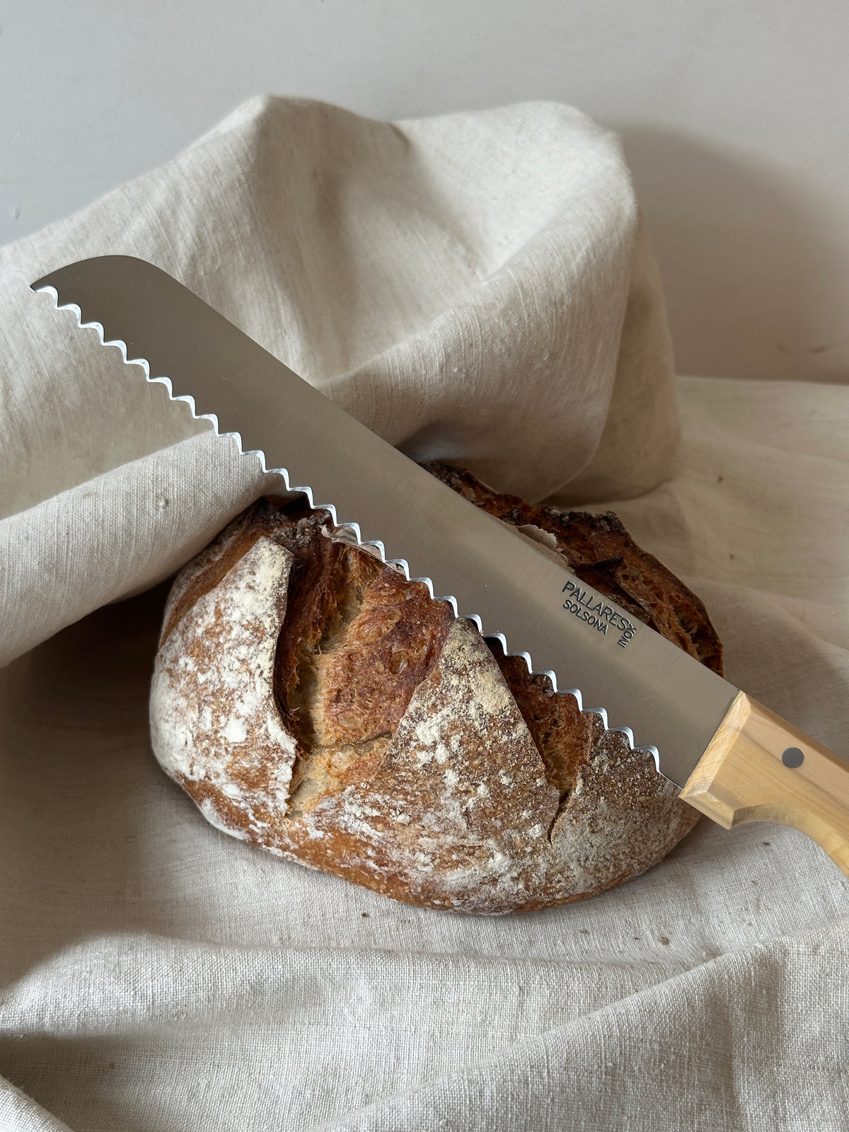 Loaf of bread with a bread knife on a light linen fabric background