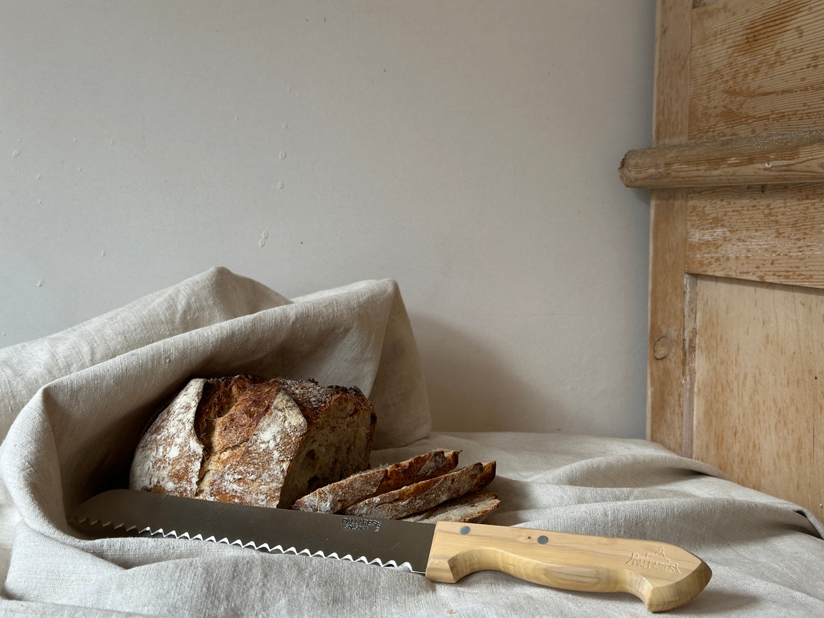Loaf of bread with a bread knife on a light-coloured cloth against a neutral background