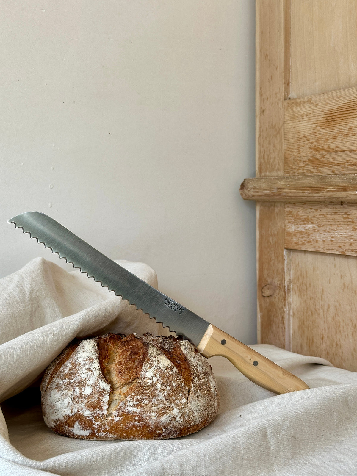Loaf of bread with a bread knife on a cloth against a wooden cupboard