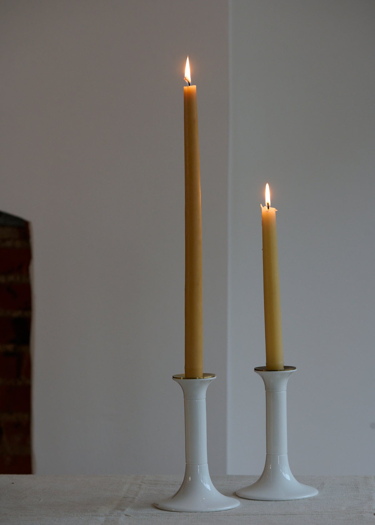 Two lit beeswax candles in white bone china candlesticks on a plain background
