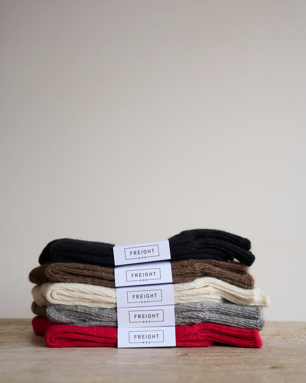 Stack of folded alpaca socks in various colours, including cream, black, brown, grey, and red, with labels in front indicating the brand.