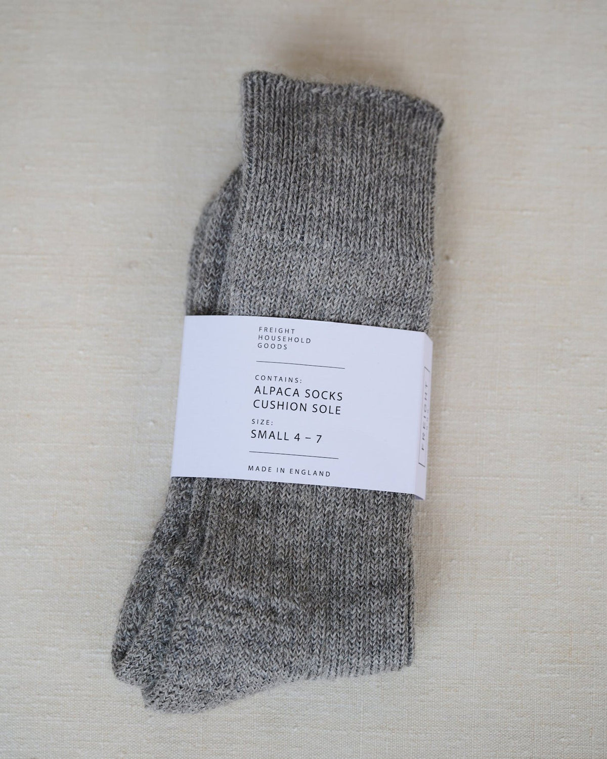 A pair of pale grey alpaca cushion sole socks with the label showing the brand name and size range.