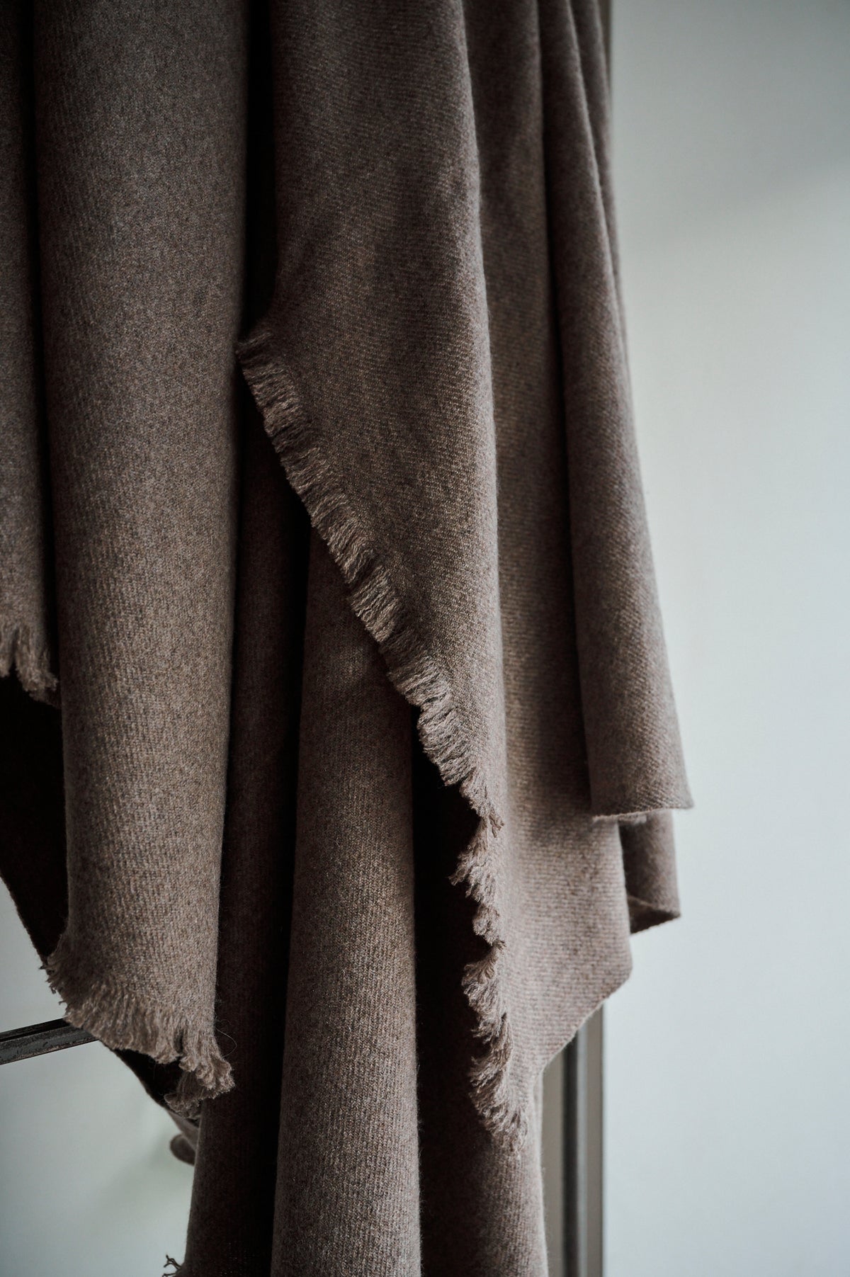 A brown undyed hand loomed cashmere bed blanket draped over a chair.