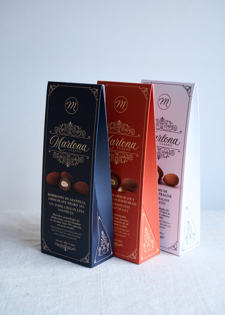 Three boxes of Marlona brand Chocolate Covered Marcona Almonds in different flavors, including Praline, Caramel with a hint of salt, and Dark Gianduja, each in a different colour box.
