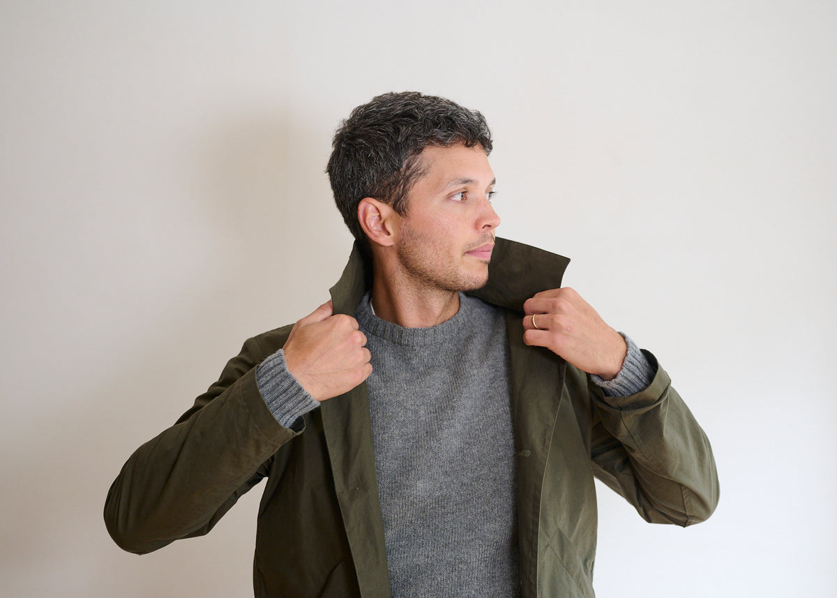 A man lifting the collar of his drywax dark olive colour duster coat