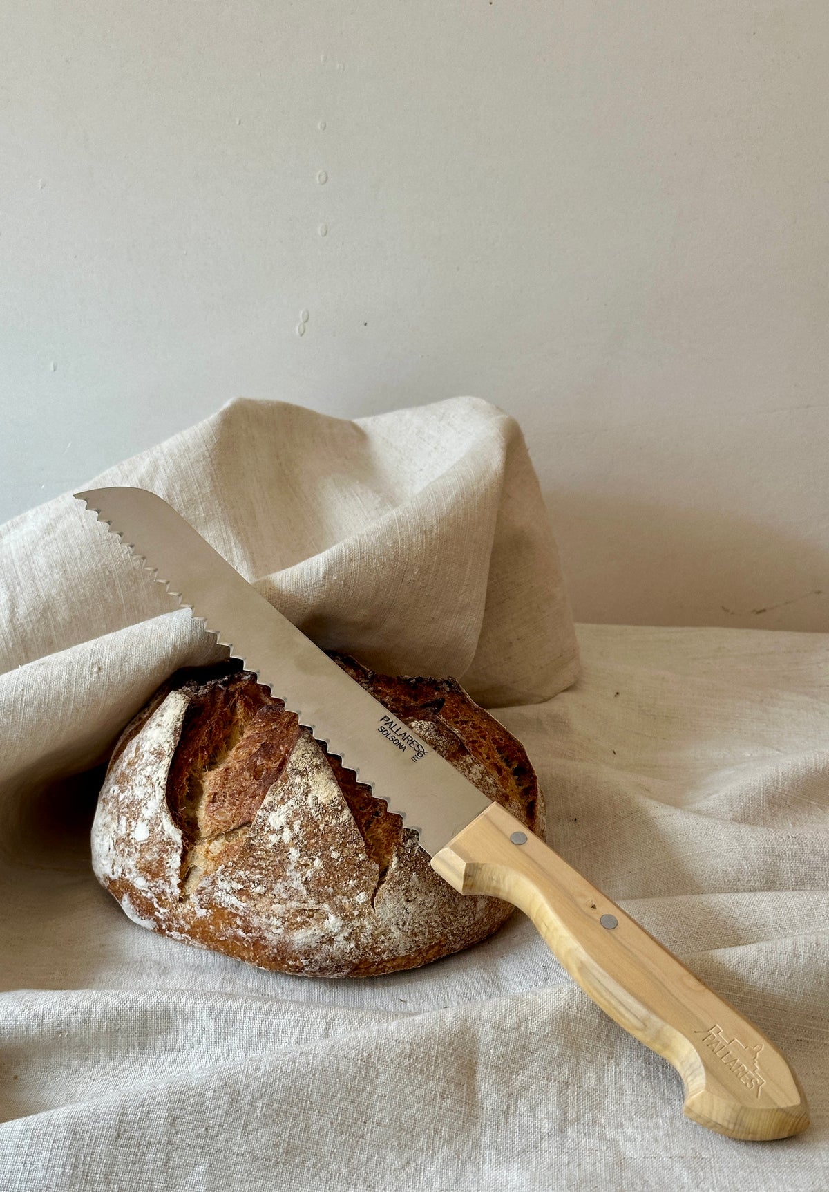 Loaf of sourdough bread with a serrated bread knife on a linen cloth