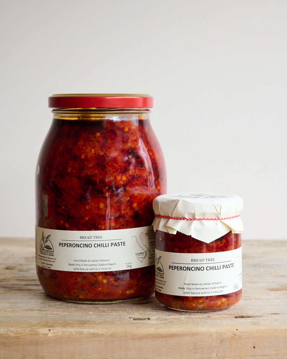 Two jars of Peperoncino Chilli tapenade, one large and one small, on a wooden surface.