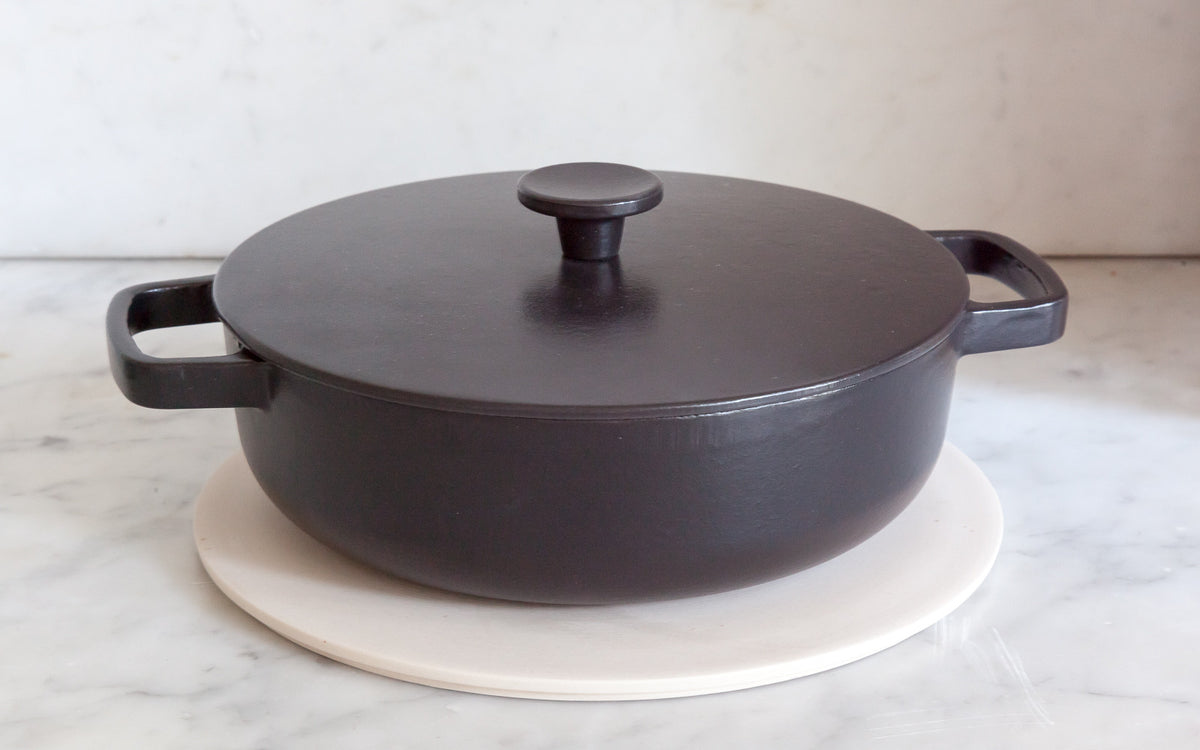 Plain Stoneware ceramic trivet with a black cast iron pan placed on top of it