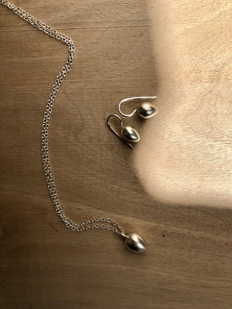 Silver necklace by Sarah King with egg shaped pendant next to matching silver egg earrings